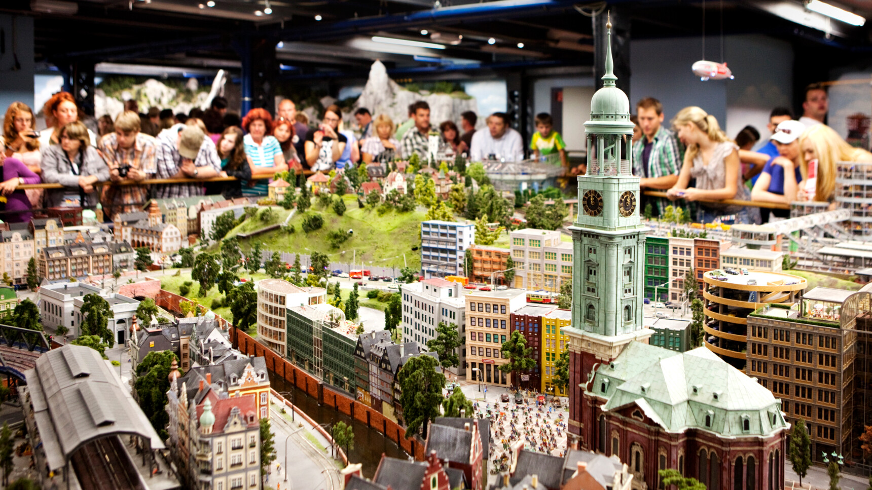 Besucher betrachten eine detaillierte Miniaturstadt mit Gebäuden, Straßen und einer großen Kirchturmuhr.