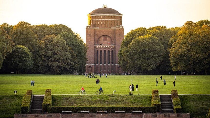 Das Planetarium Hamburg mit umliegender Parkwiese und Menschen beim Spazieren und Radfahren.