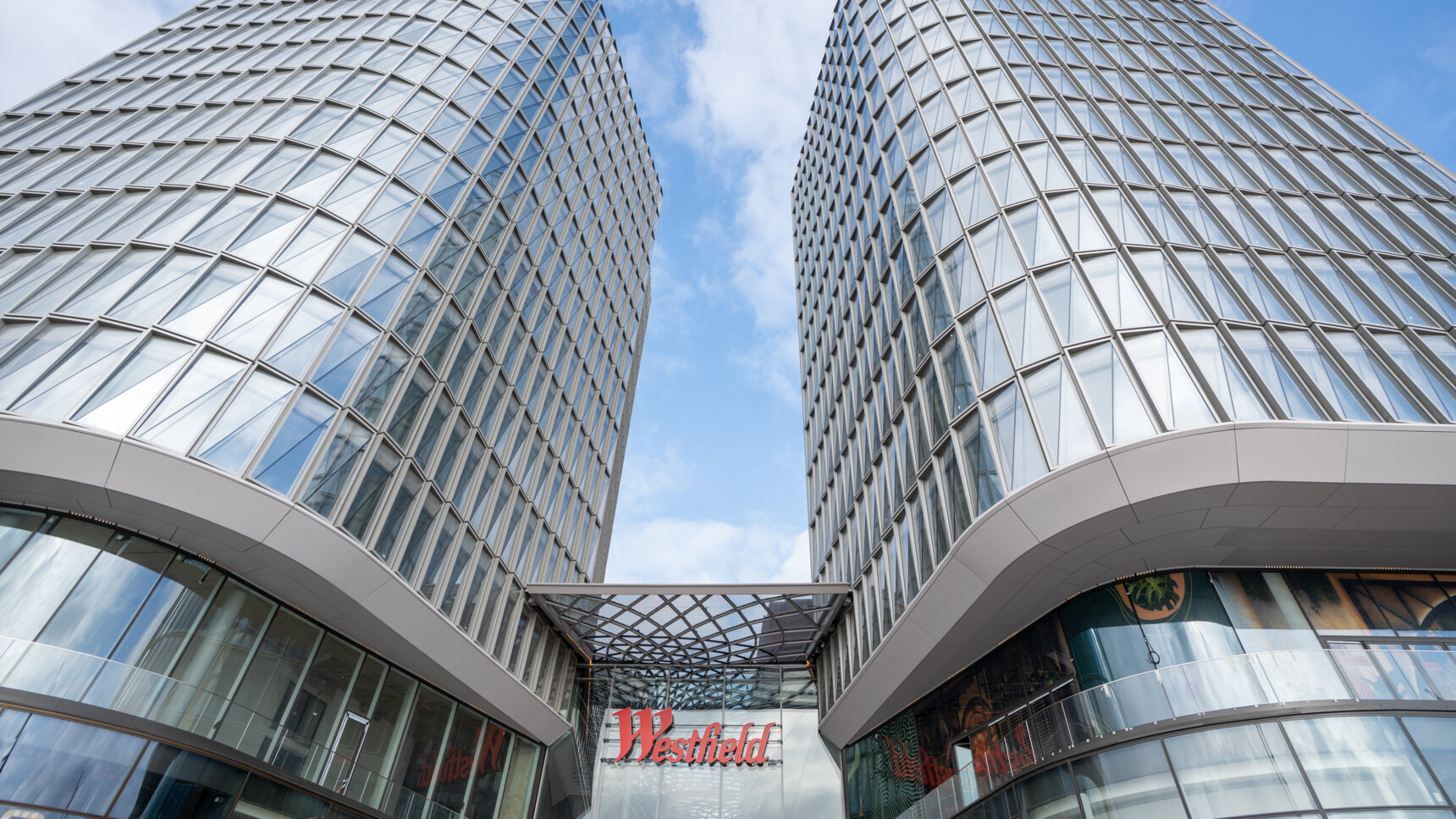 Blick nach oben auf zwei moderne, glasverkleidete Hochhäuser mit dem Schriftzug „Westfield“ dazwischen.