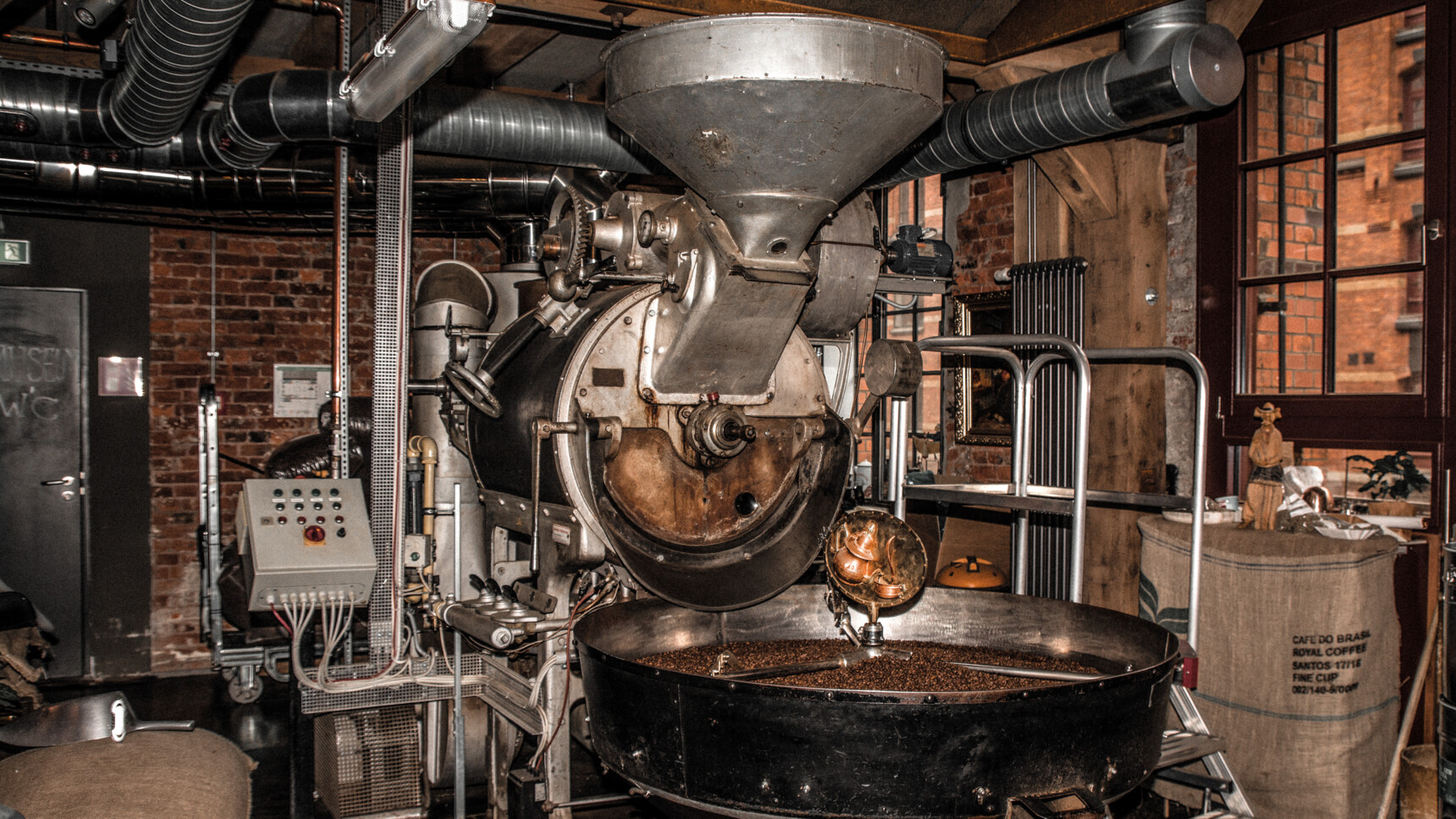 Industrielle Kaffeeröstmaschine in einer rustikalen Kaffeerösterei mit Backsteinwänden.