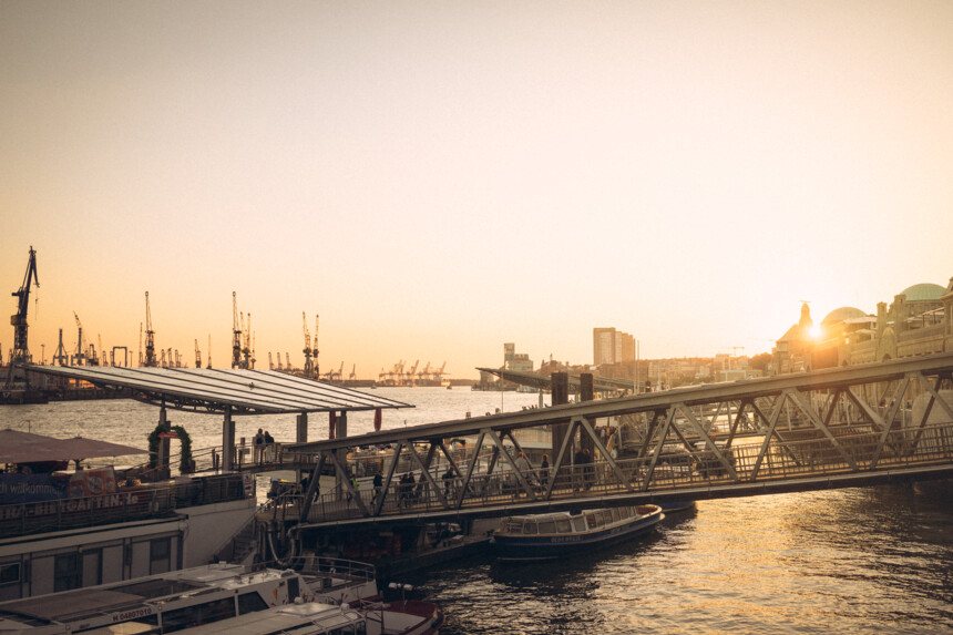 Sonnenuntergang über dem Hamburger Hafen mit Kränen, Brücke und Booten im Wasser.