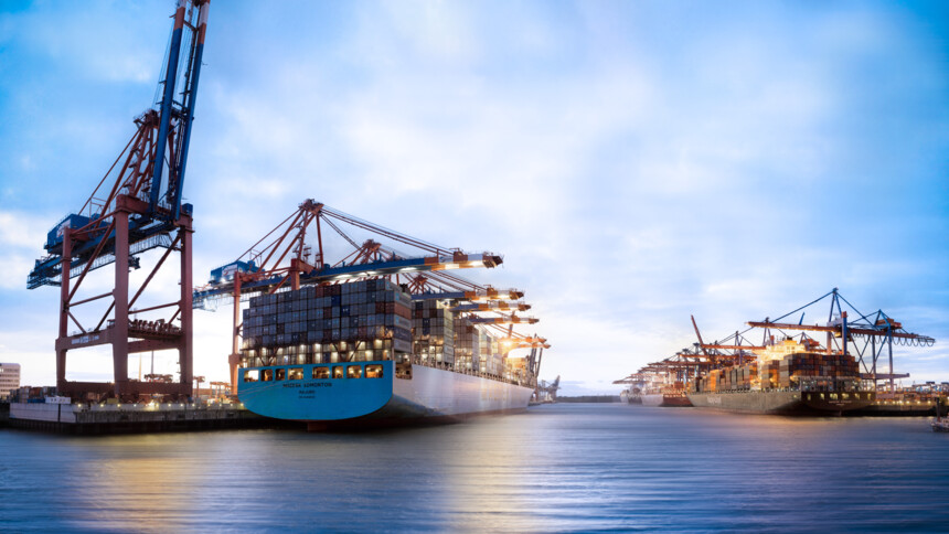 Containerschiffe werden in einem Hafen bei Dämmerung mit Kränen beladen.