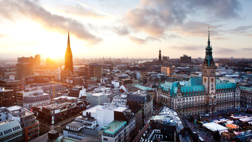 Luftaufnahme von Hamburg bei Sonnenuntergang mit Rathaus und Elbphilharmonie im Hintergrund.
